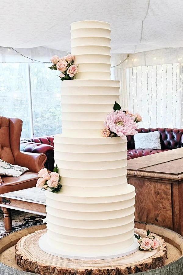 4 tier buttercream wedding cake. White chocolate ganache covering, with scalloped edging design, and fresh flowers.
